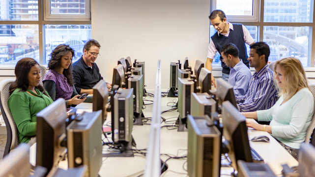 Trainer begeleidt een groep medewerkers in een computerlokaal