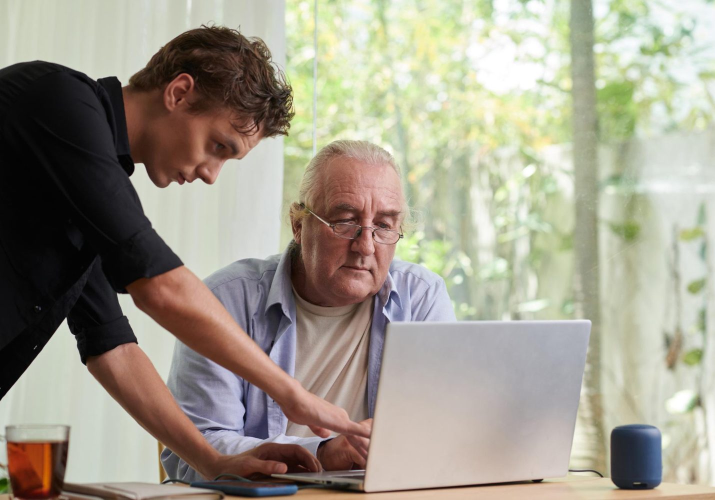 Trainer legt geduldig iets uit aan een oudere deelnemer achter de laptop